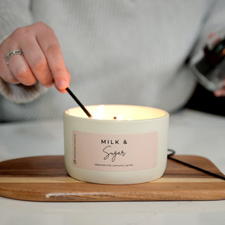 Candle labeled 'Milk & Sugar' being lit on a wooden coaster.