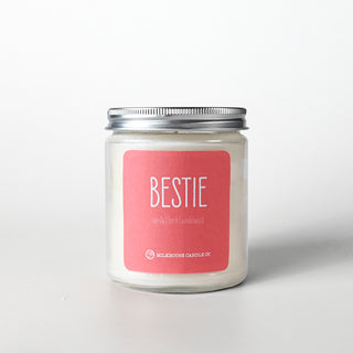 Candle in a clear jar with silver lid labeled 'BESTIE' on a pink label against a white background