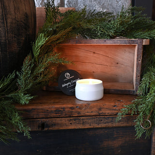 Candle on a wooden surface with greenery and a wooden box in the background