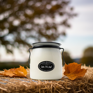 White jar with a black lid and 'Rake, Pile, Leap!' label on a hay bale with autumn leaves, blurred trees in the background