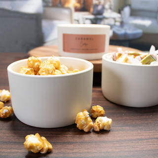 Caramel popcorn in white ceramic bowls with ceramic candle in background labeled 'Caramel Corn'