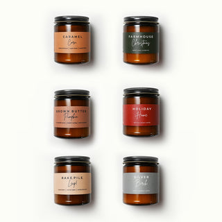 Set of six candles in amber jars with labeled scents on a white background