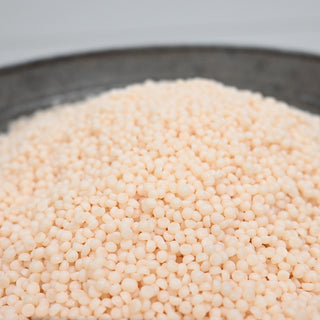 Close-up of small beige wax beads in a metal container with a white background
