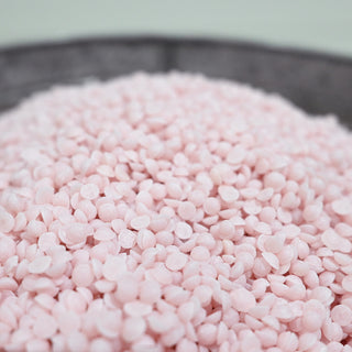 Close-up of pink scented wax beads in a metal container with a white background