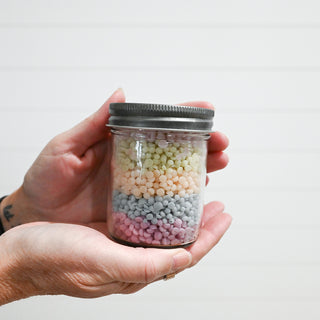 Hand holding a jar of multicolored wax beads against a plain background