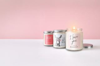 Three candles with different labels on a white surface and pink background