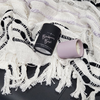 a blackberry and basil candle and its tube layed on a fringe blanket 