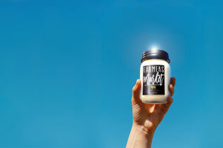 Hand holding a jar labeled 'Farmers Market' against a clear blue sky