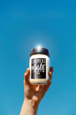 Hand holding a jar labeled 'Farmers Market' against a clear blue sky