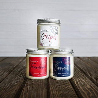 Three candles with labels 'Stars & Stripes', 'Fireworks & Freedom', and 'White & Boom' on a wooden surface.