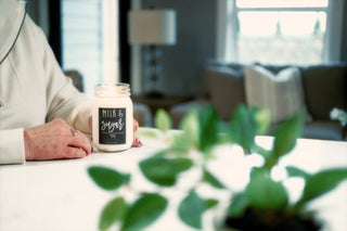 Person holding a 'Milk & Sugar' clean burning soy candle in a living room setting