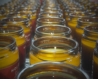 Rows of glass amber jars with candles inside, shortly after being poured