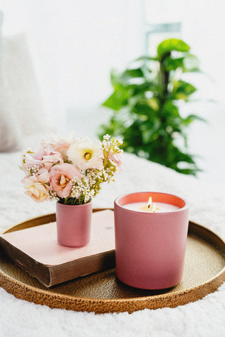 Pink ceramic candle lit on a tray with the votive of the same pink vessel filled with flowers  