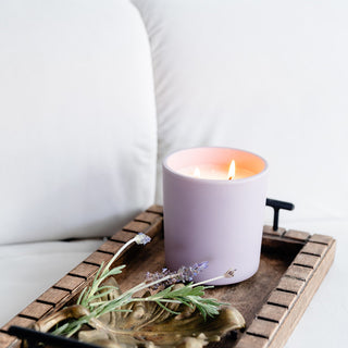 a lavender lit candle on a try with some lavender on a white couch 