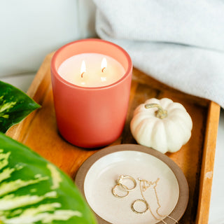 an tiger orange lit candle on a tray with a keeps dish with a couple rings, neckalace, and pumpkin 
