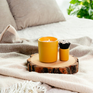 a yellow ceramic candle tumbler with a matching votive that has black matches 