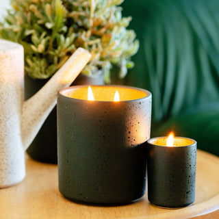 a lifestyle image of sandalwood and fir in both the tumbler and the votive in the flecked dark green ceramic  vessel candles 