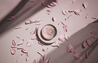 a pink bone china candle sitting on a saucer with pink petals laid about 