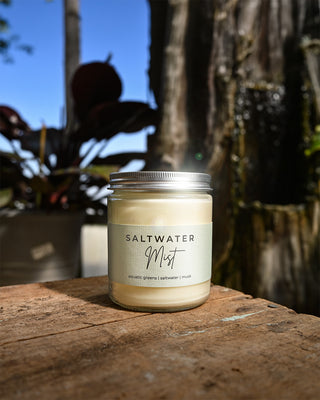 Candle labeled 'Saltwater Mist' on a wooden surface with plants in the background